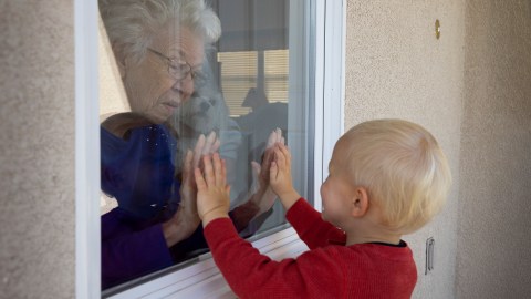A little boy finding lockdown compensation by reaching out to an old lady through a window.