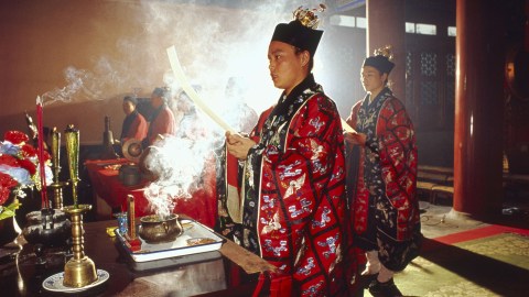 A man in a Chinese costume is holding a candle, exemplifying the essence of Taoism.
