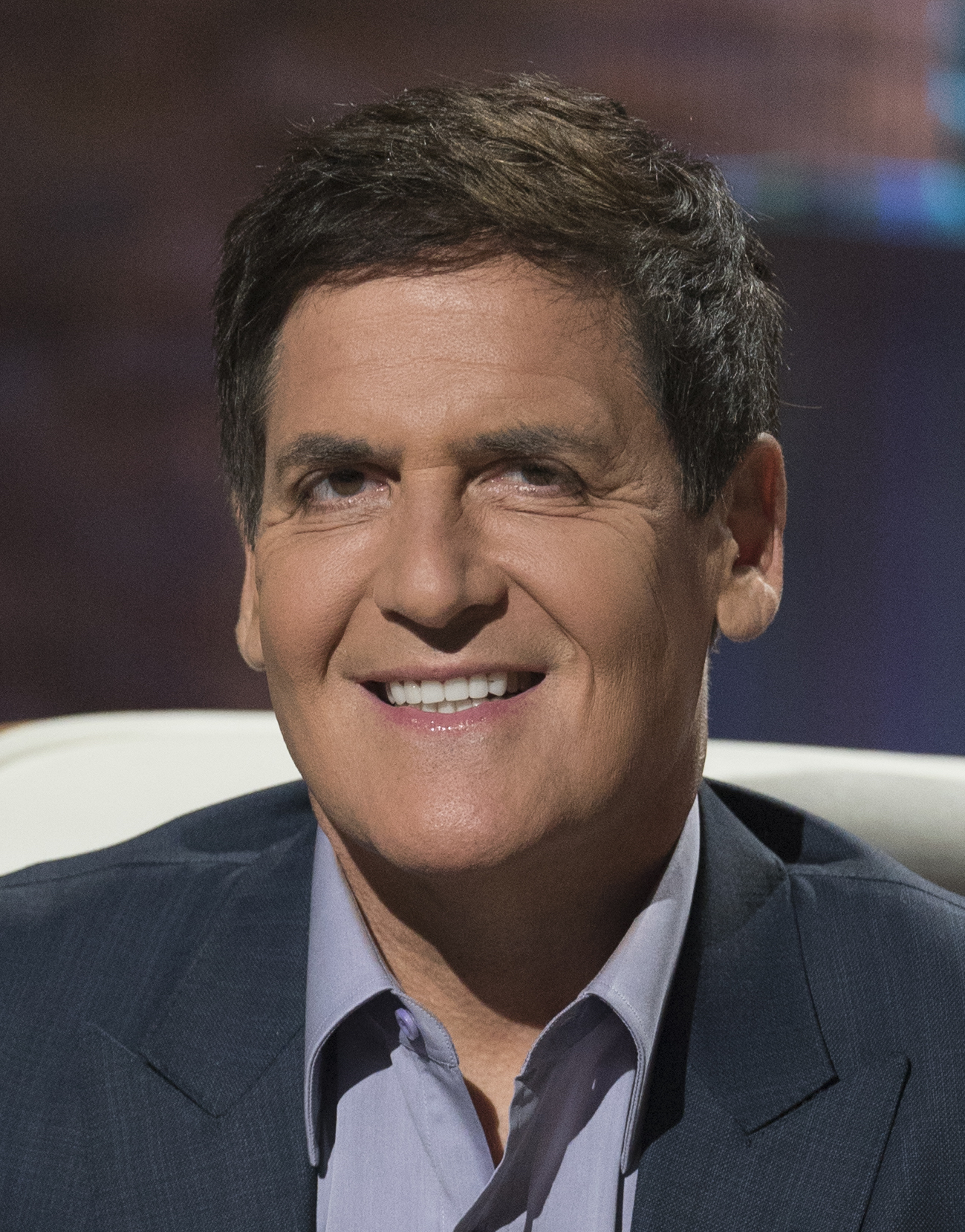 A smiling man in a suit sitting on a chair.