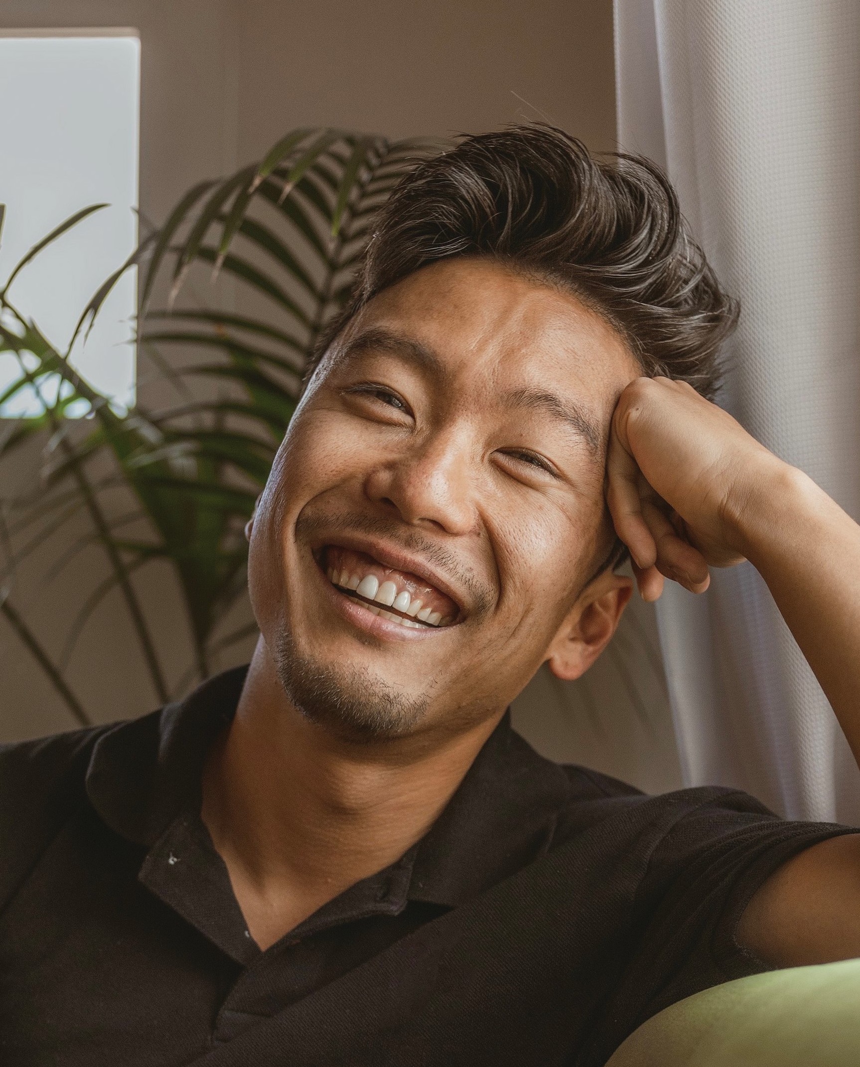 A smiling asian man sitting on a couch.