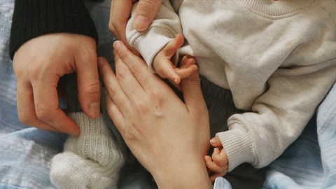 A woman holding a baby's hand, symbolizing the bond between families.