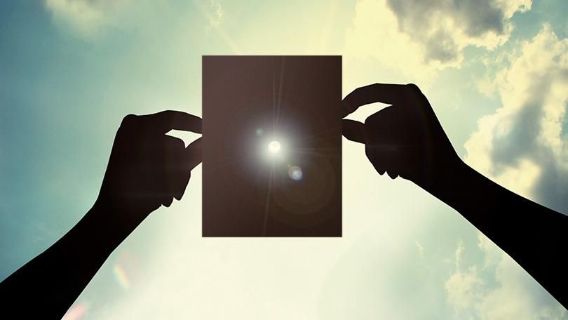 A pair of hands holding a piece of paper in front of a blue sky, symbolizing the vast distance to the stars.