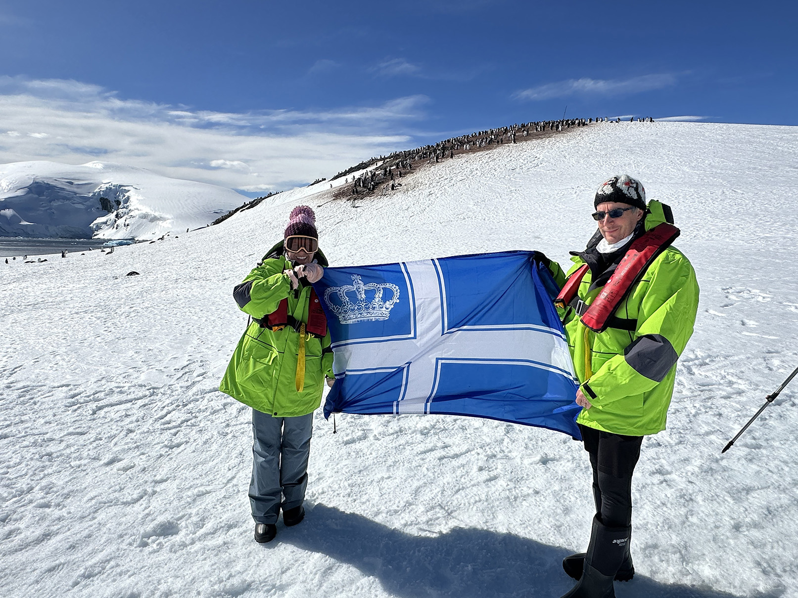 Two people holding a flag in the snow on an antarctic mountain.