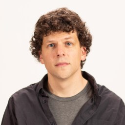 A man with curly hair is standing in front of a white background.