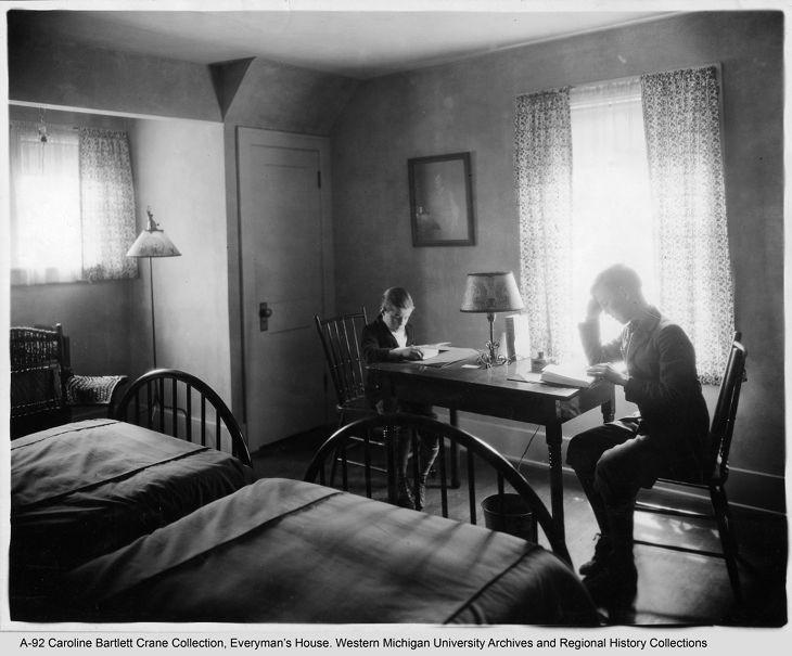 A black and white photo of a room with two beds and a desk.