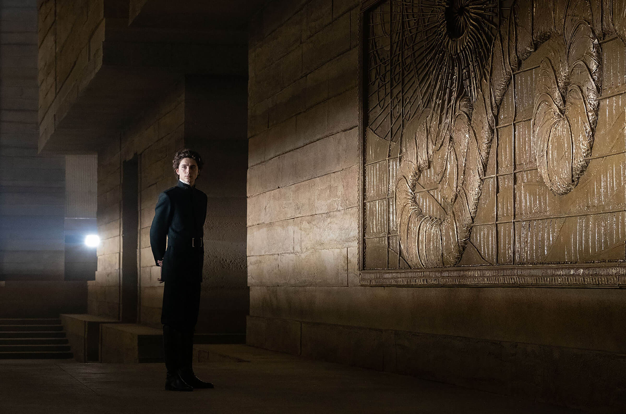 Man standing in a dimly lit hallway with ornate wall carvings.