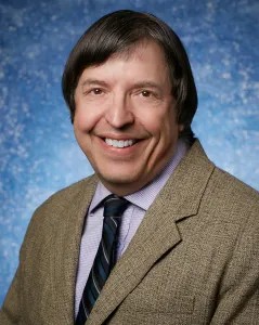 Professional portrait of a man in a suit and tie with a blue speckled background.