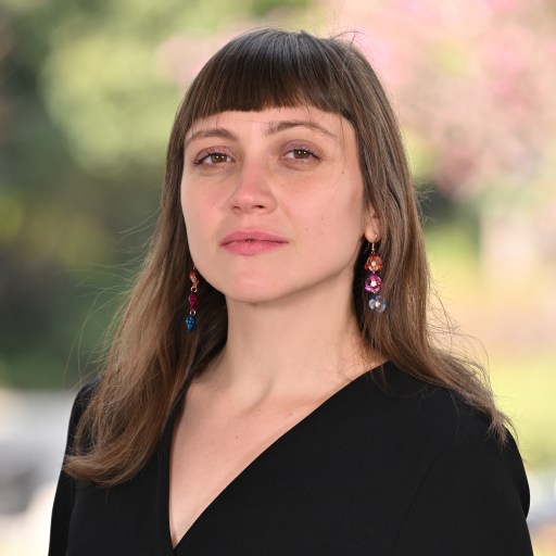 Woman with bangs wearing earrings and a black top posing for the camera.