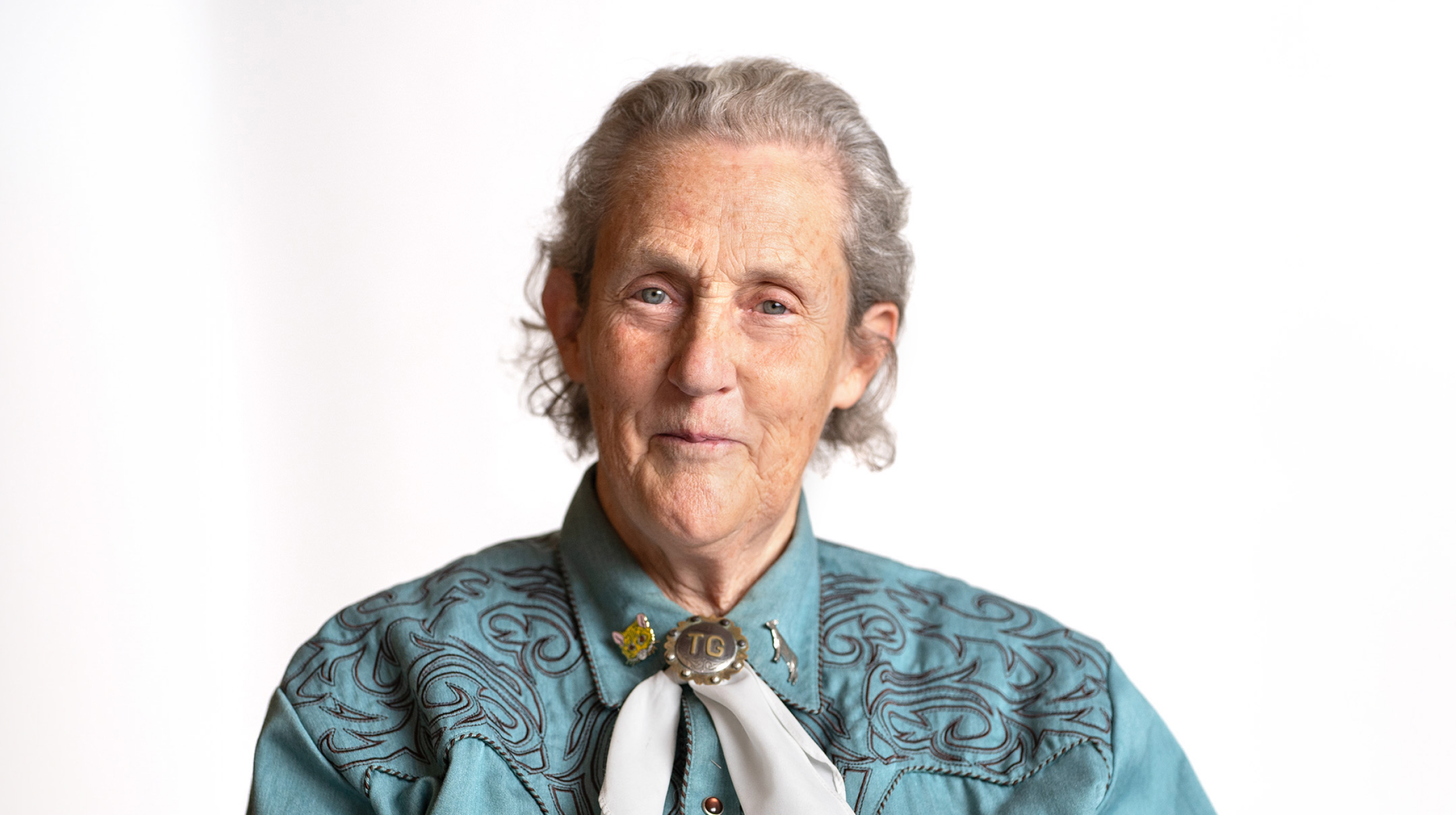 Elderly woman with a gentle smile wearing a turquoise blouse and a neck scarf.