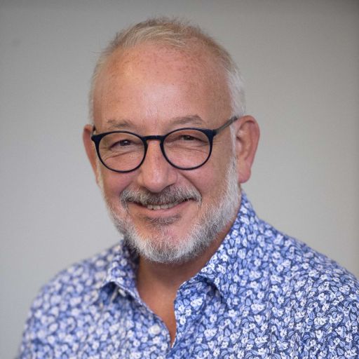 A smiling man with glasses, a beard, and a patterned shirt.