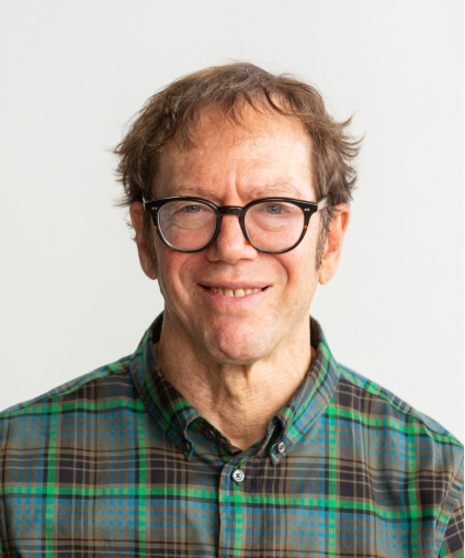 Middle-aged man with glasses smiling, wearing a plaid shirt against a gray background.