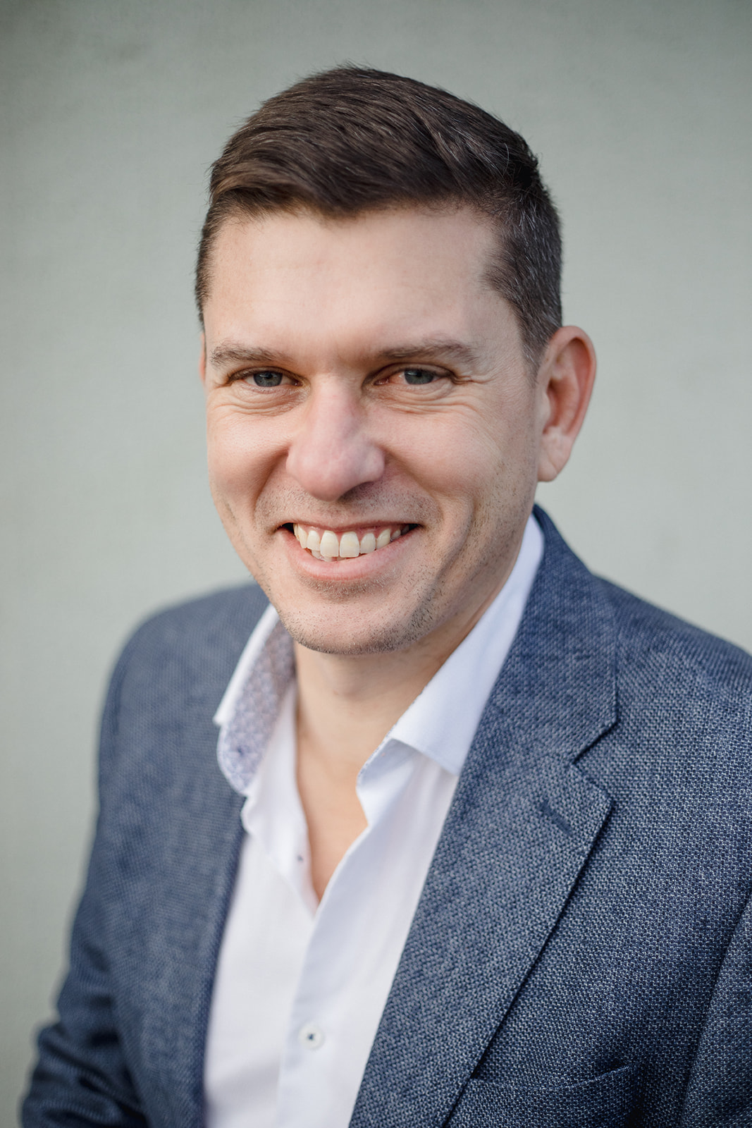 A smiling man in a blue blazer and white shirt against a neutral background.