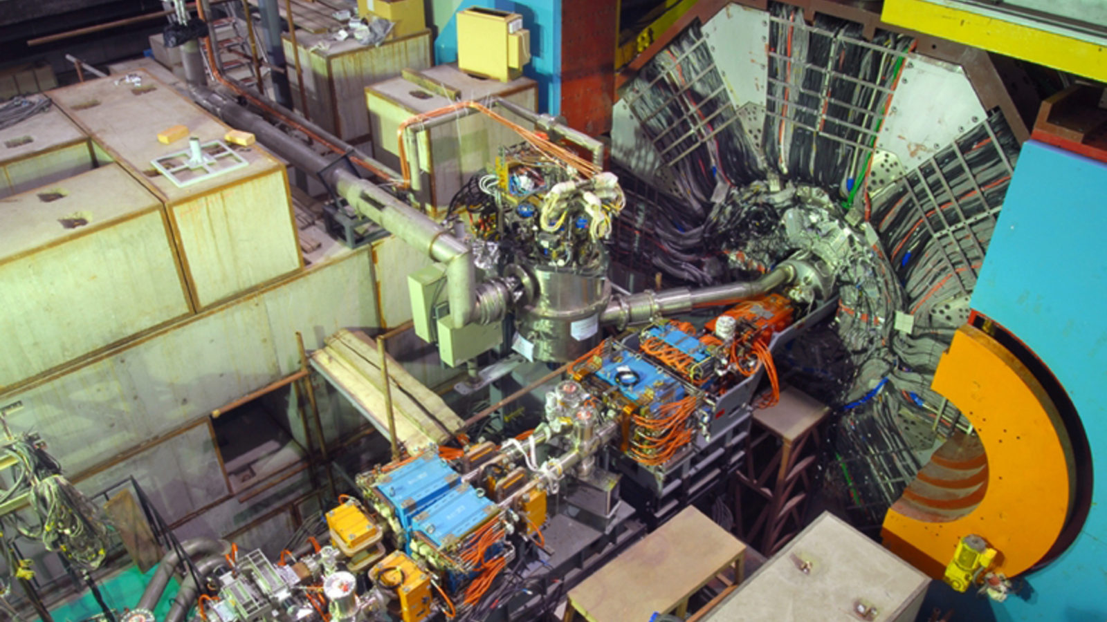 Interior of a particle physics laboratory showing a complex particle accelerator setup with multiple cables, detectors, and machinery designed to study glueball particles.