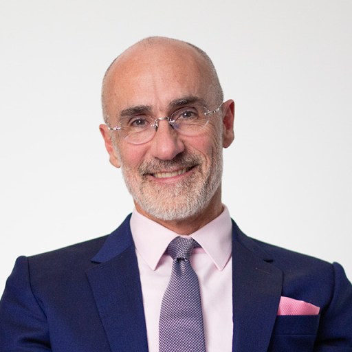 Bald man with glasses wearing a suit and tie, smiling at the camera against a plain background.