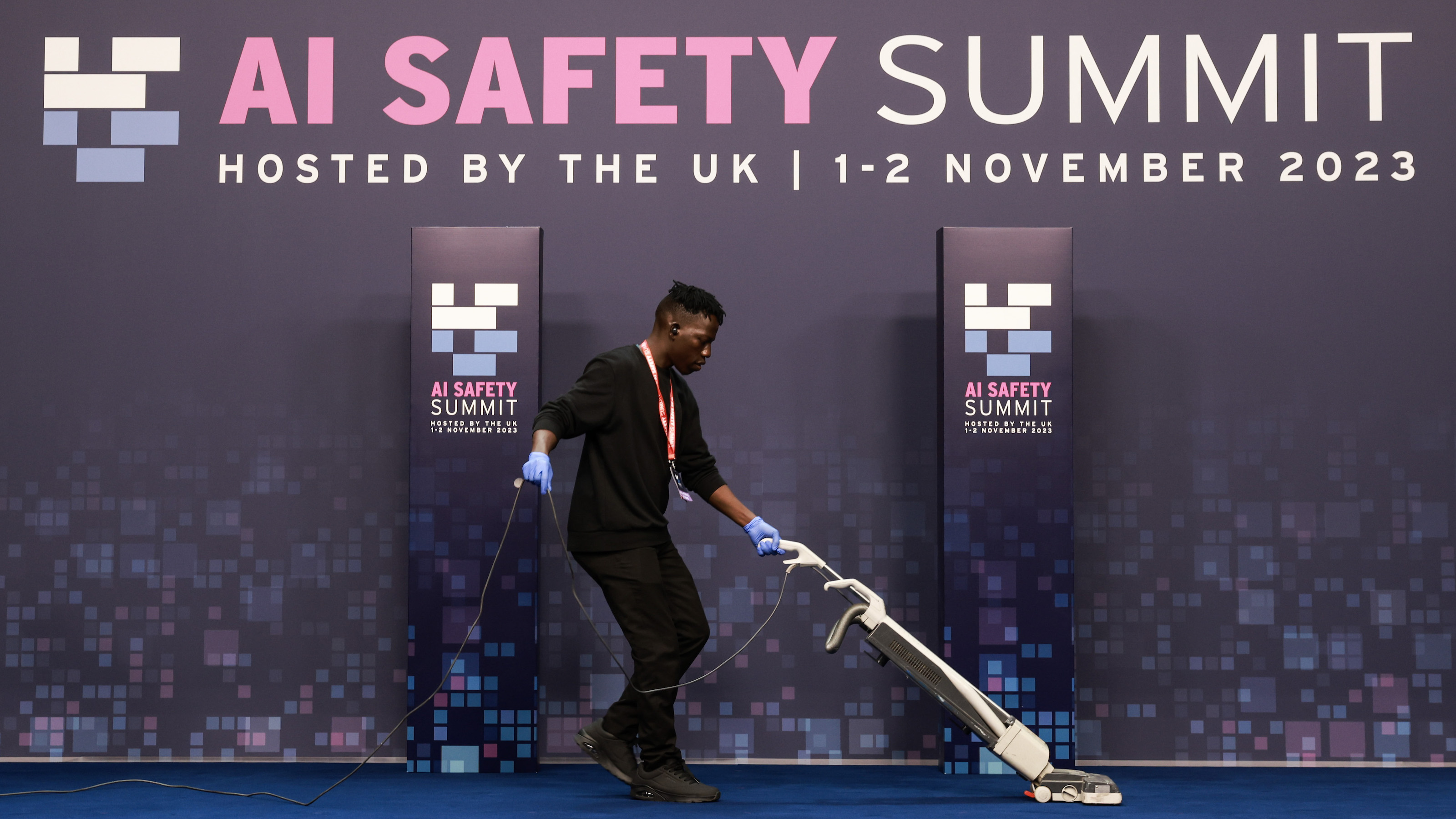 A person vacuuming a blue carpet at the AI Safety Summit hosted by the UK on November 1-2, 2023, where discussions on agentic AI took center stage.