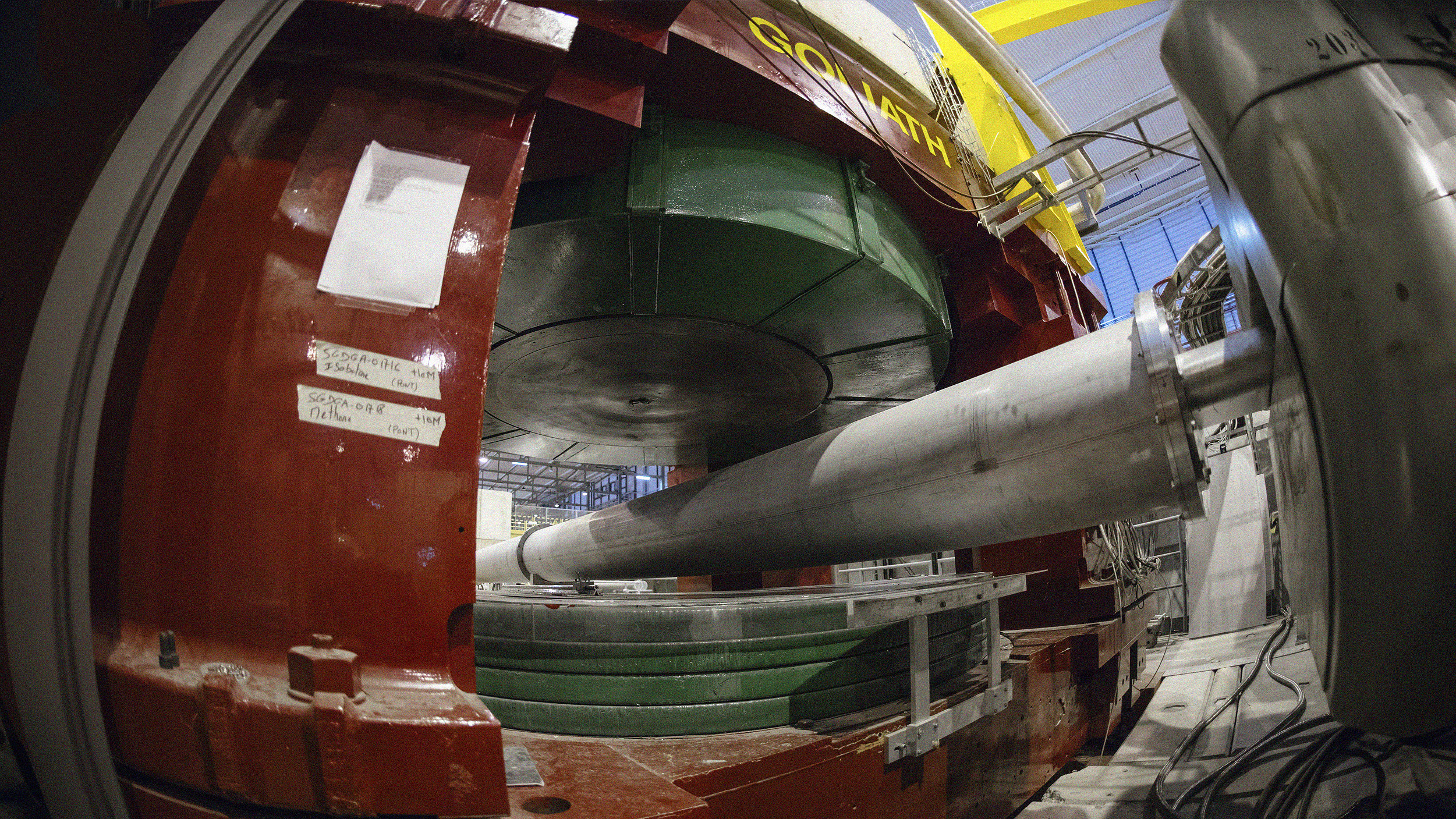 Image of a large industrial machine with a green cylindrical component and a long metal rod inside a red and gray structure.