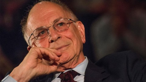 Kahneman wearing a suit, rests their chin on their hand while looking thoughtfully ahead.