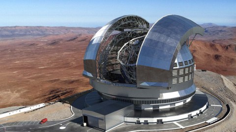 A large astronomical observatory, featuring the futuristic dome structure of an ELT, stands majestically in a desert landscape. A small red vehicle is visible near the base of the observatory.