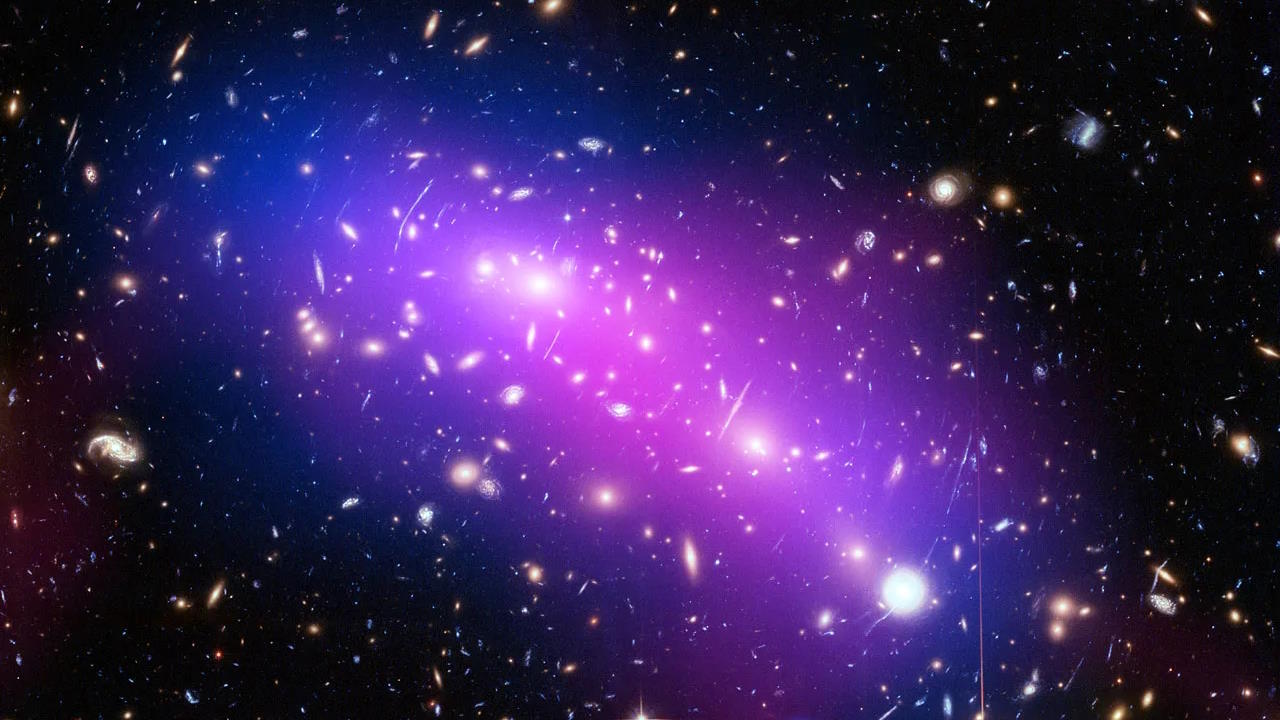 Image of a galaxy cluster with a purple haze showing dark matter, surrounded by numerous distant stars and galaxies against the dark backdrop of space.