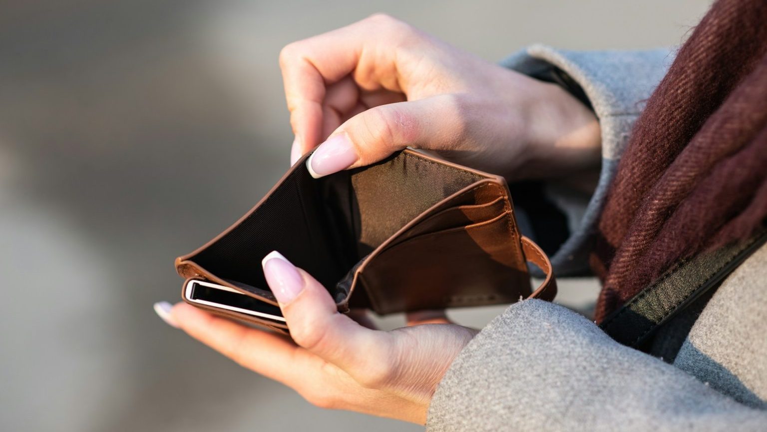 Person holding an open, empty brown wallet with both hands, outdoors.