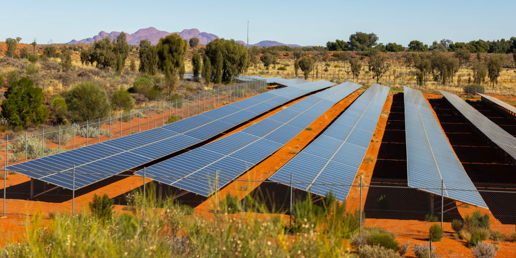 Array of solar panels installed in a fenced area in a desert landscape with mountains in the background.