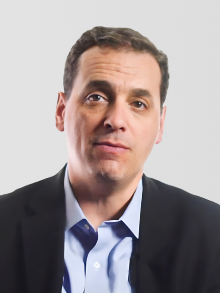 A man with short brown hair wearing a blue shirt and dark blazer is looking slightly off-camera against a plain light background.