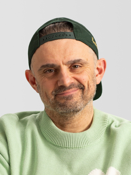 A person wearing a green cap backward and a green sweater, smiling slightly, with a light gray background.