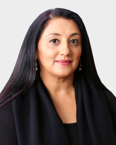 Portrait of a woman with long, dark hair wearing a black top and earrings, facing forward with a neutral expression, set against a plain background.