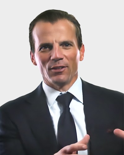 A man in a suit and tie is speaking, gesturing with his hand.