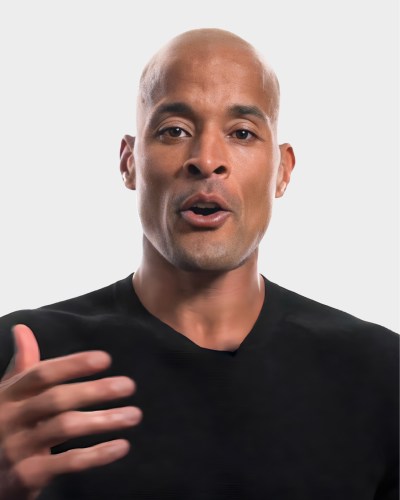 Bald man in a black shirt gestures with his right hand, speaking against a plain white background.