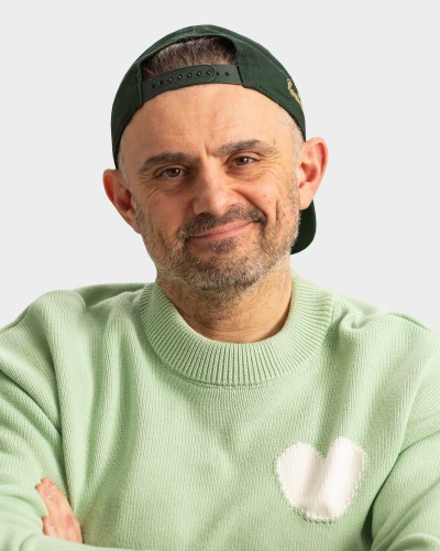 A person is wearing a backward green cap and a light green sweater with a white heart design, smiling and looking directly at the camera.