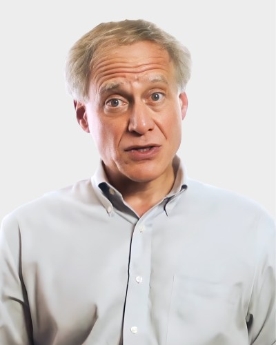 Man with light-colored hair and a receding hairline is wearing a light-colored button-up shirt and looking directly at the camera, with a neutral to slightly surprised expression. Plain white background.