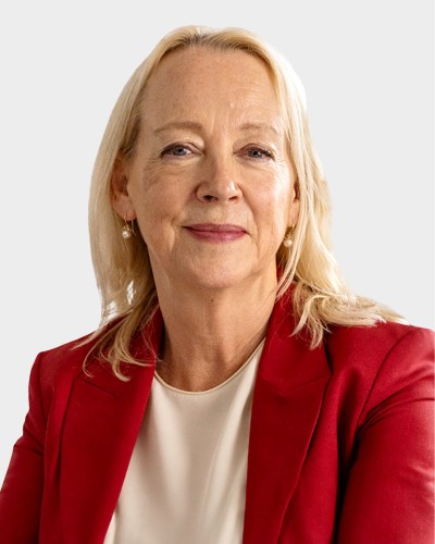 A woman with long blonde hair wearing a red blazer and a white blouse is smiling slightly, looking at the camera.