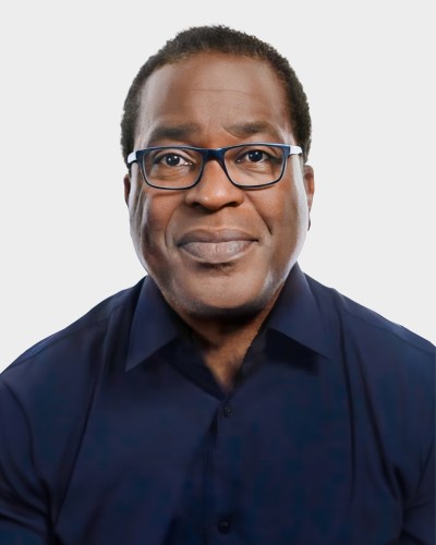 A person wearing glasses and a dark blue shirt looks directly at the camera against a plain white background.