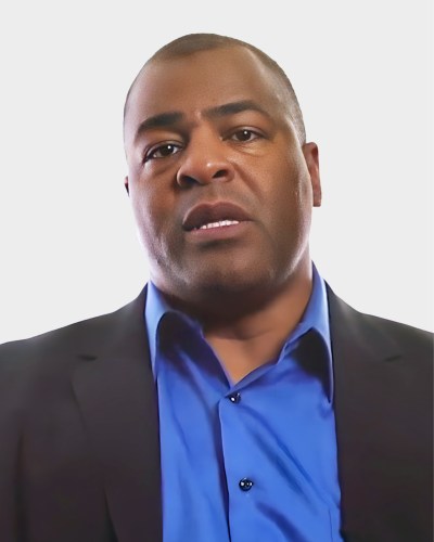 A person wearing a blue shirt and dark jacket stares ahead against a plain white background.