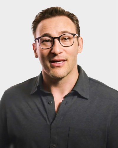 A person with short dark hair, glasses, and a dark button-up shirt is smiling at the camera against a plain white background.