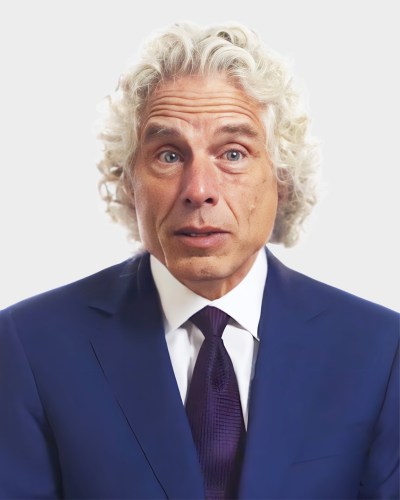 A man with curly white hair, wearing a dark blue suit and a matching tie, poses against a plain white background.