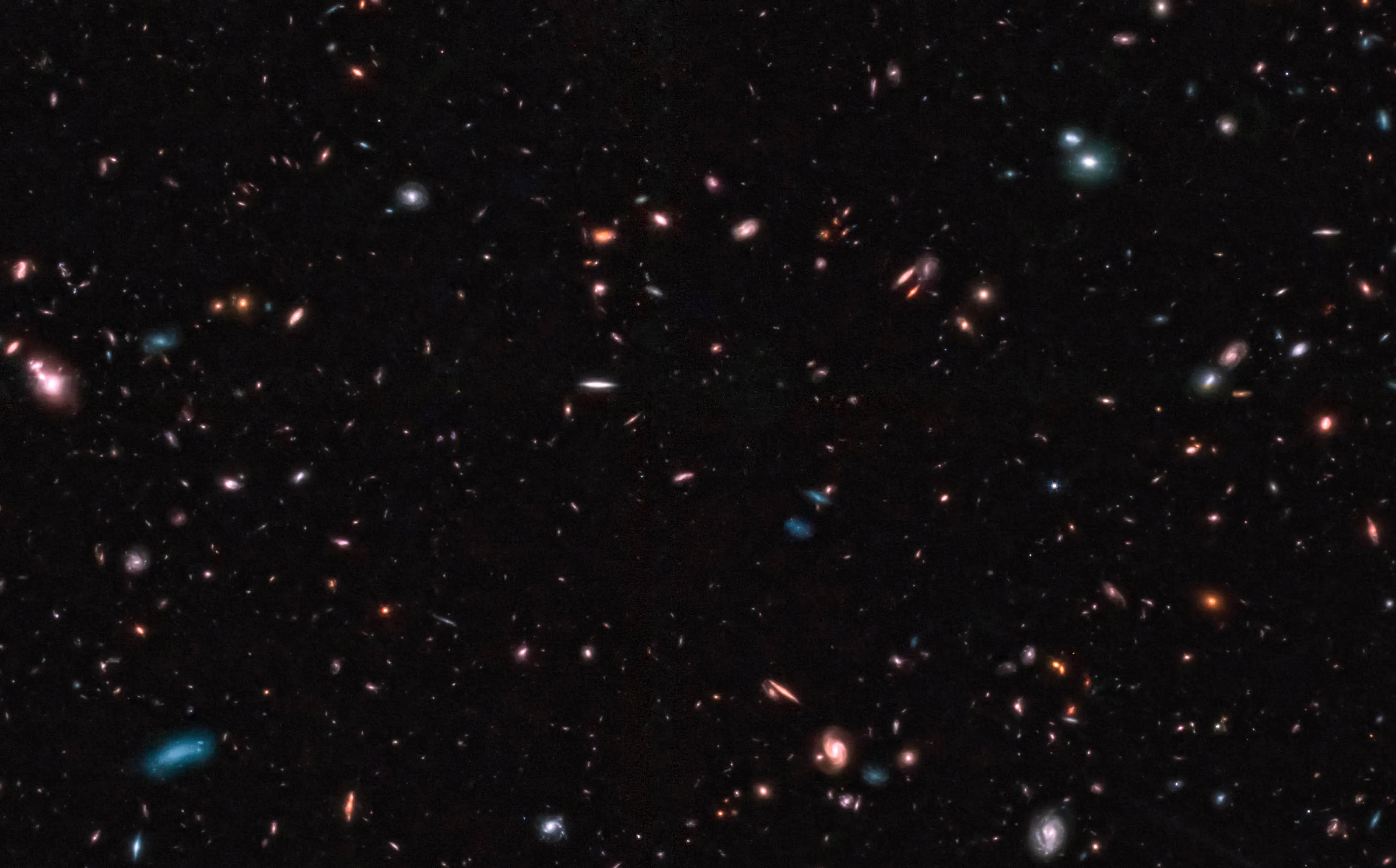 A deep-space image captured by the JWST showcases numerous galaxies of various shapes, sizes, and colors scattered across a dark background, potentially setting a new cosmic distance record.