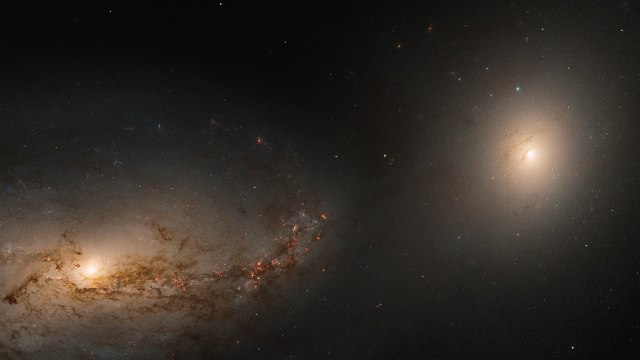 A detailed image of two galaxies in space, one with spiral arms on the left and the other, more elliptical, on the right, surrounded by distant stars.