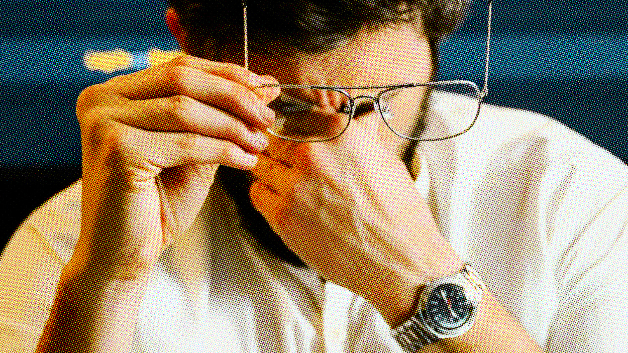 A man rubs his eyes while holding his glasses in his left hand and wearing a white shirt, with a watch on his left wrist, perhaps tired from hours of Zoom science sessions.