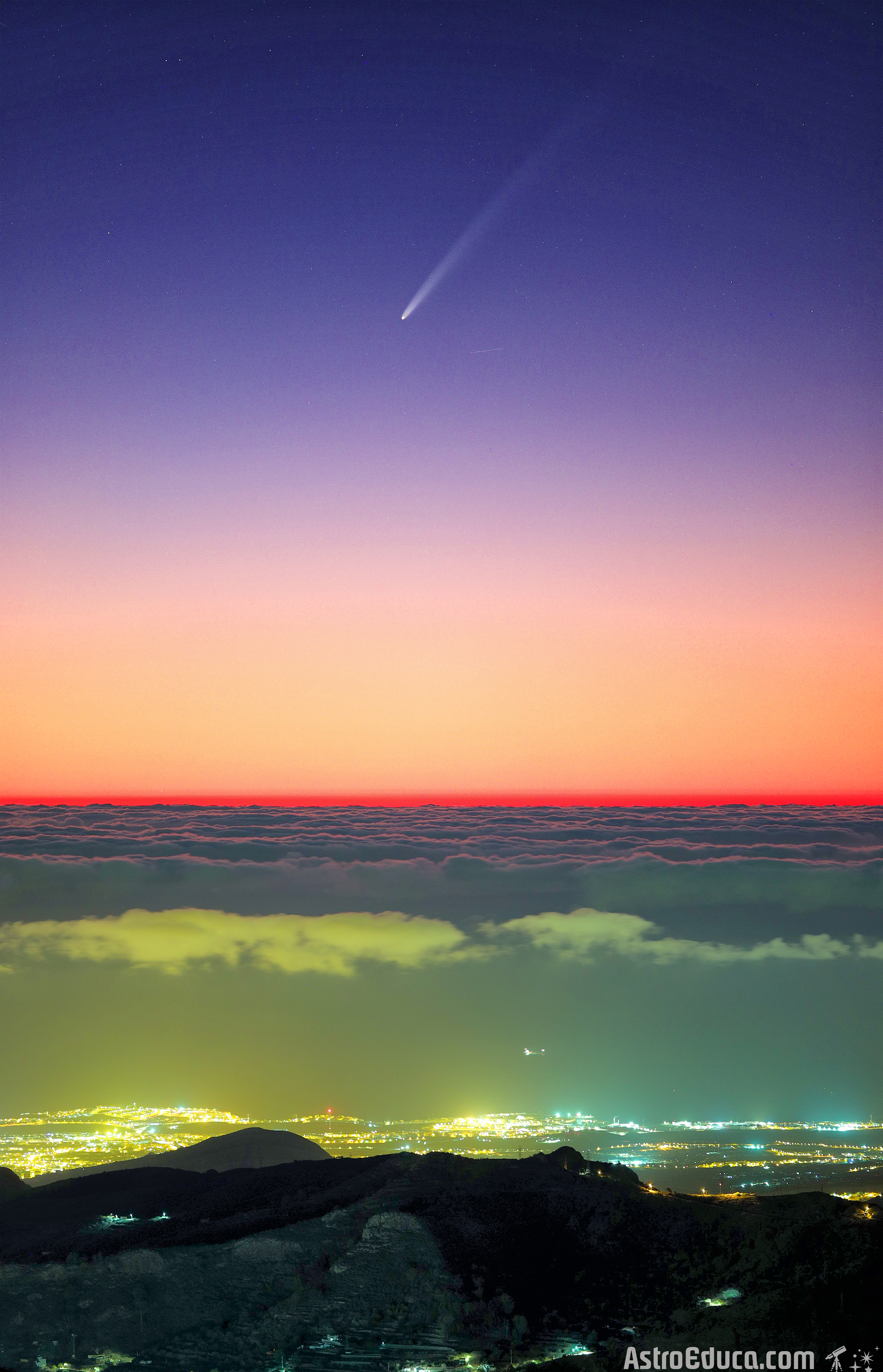 A sunset sky with a visible comet above a cityscape. The horizon shows a gradient from orange to deep blue with city lights illuminating the terrain below.