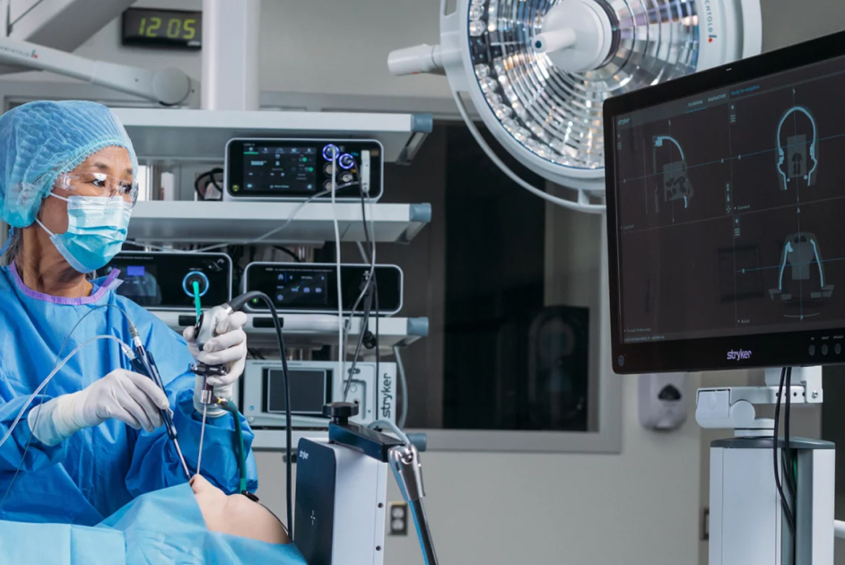 A medical professional in surgical attire operates equipment while observing a monitor displaying patient scans in an operating room.