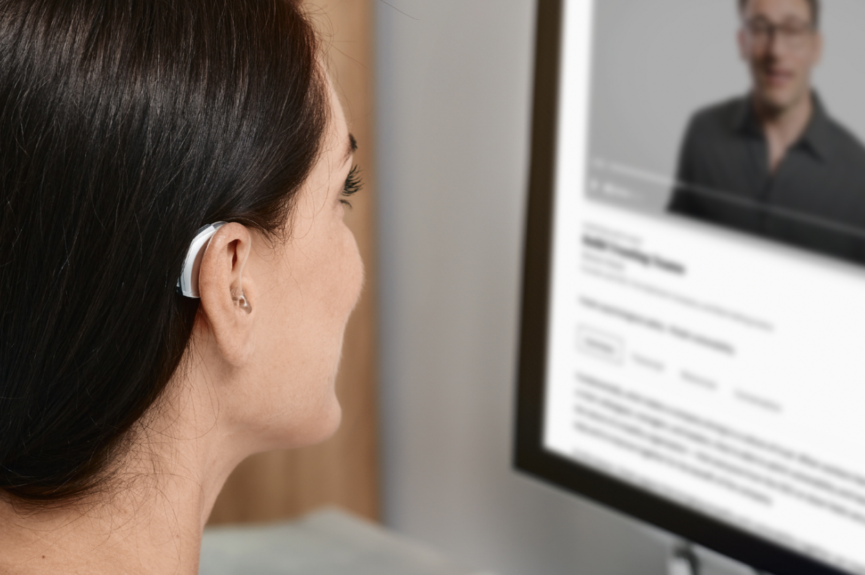 A woman with a hearing aid watches a video on a computer screen.