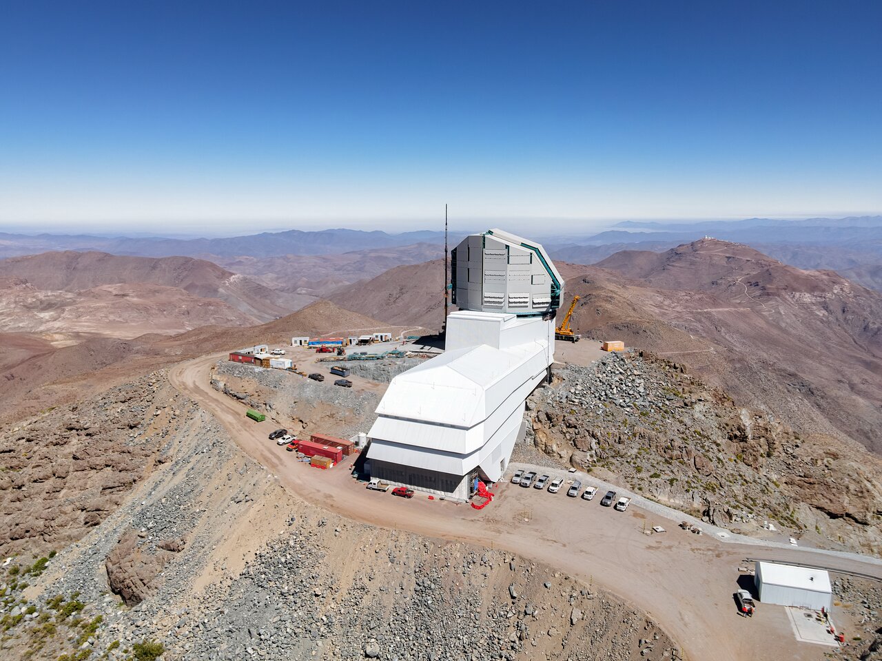 A large observatory with a white structure is situated on a rocky mountain landscape under a clear blue sky, renowned as one of the best astronomy locations on Earth. It is surrounded by desert terrain and scattered buildings, providing an ideal vantage point for celestial observations.