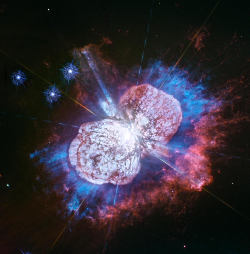 A vivid image of the Eta Carinae nebula reveals a mysterious and bizarre display of bright blue, red, and pink clouds of gas and dust surrounding a central star, set against a dark space background.