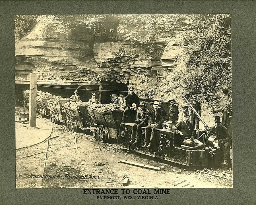 Historic photo of miners sitting on coal carts at the entrance of a coal mine in Fairmont, West Virginia.