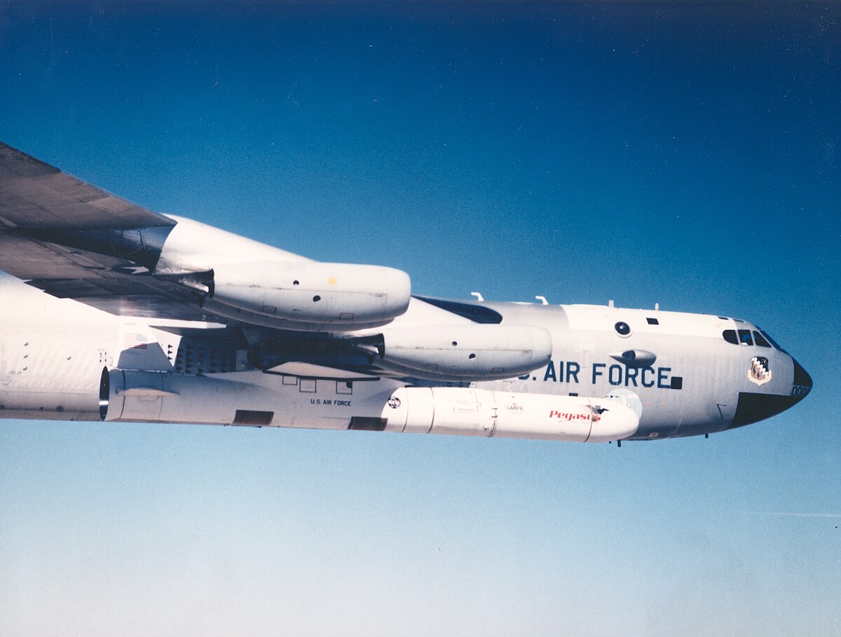 A U.S. Air Force aircraft with a large missile attached underneath flies against a clear blue sky.