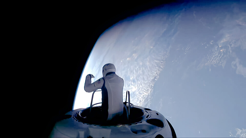 A person in a spacesuit stands at the hatch of a spacecraft, looking at Earth from space.