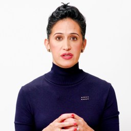 Person with dark hair in a bun, wearing a black turtleneck, stands against a white background. BT+ logo is in the top right corner.