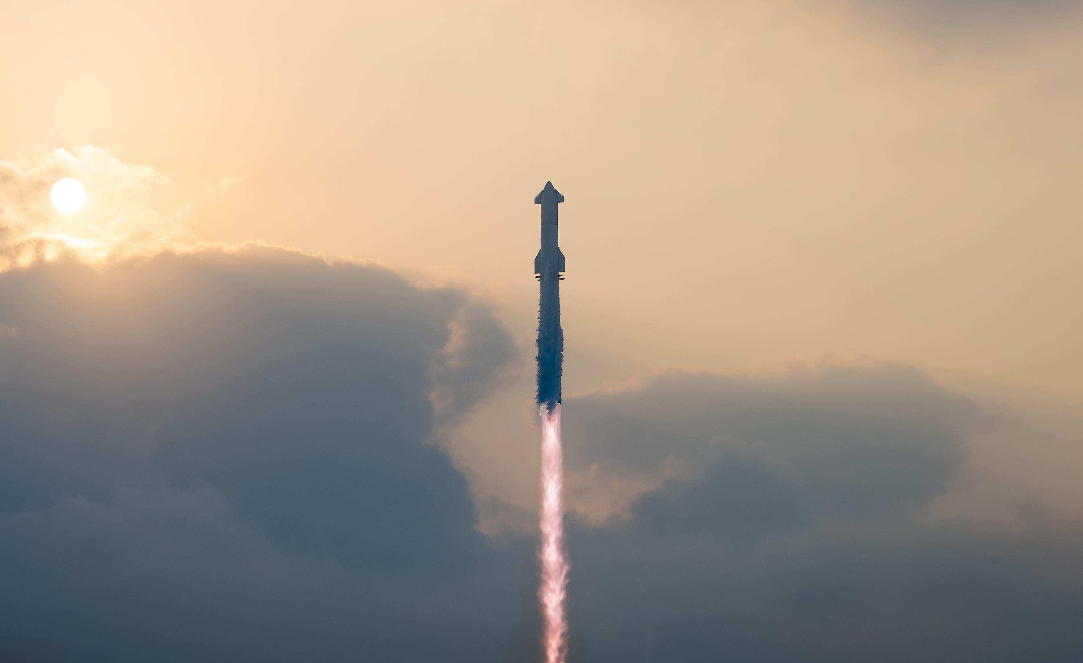 A rocket launches into the sky against a cloudy backdrop, with the sun partially visible.